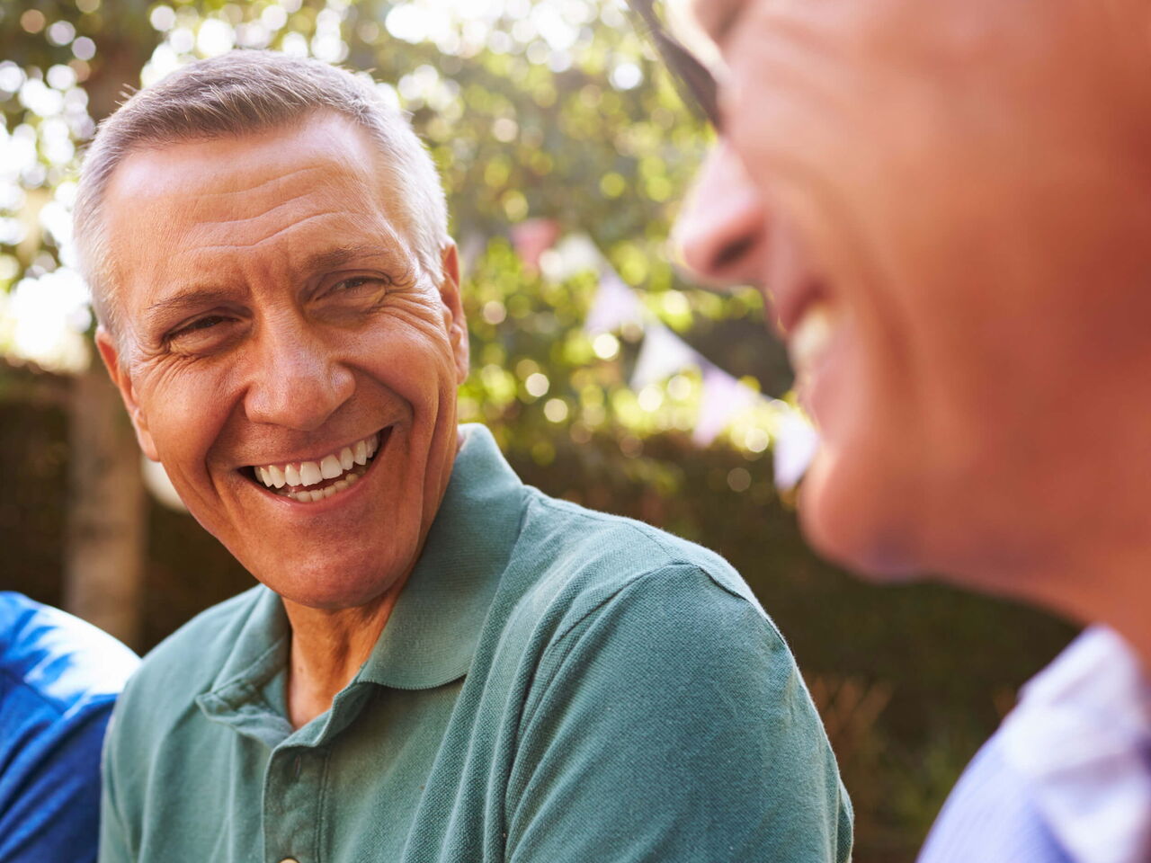 Ältere Männer sitzen in einem Garten und lachen.